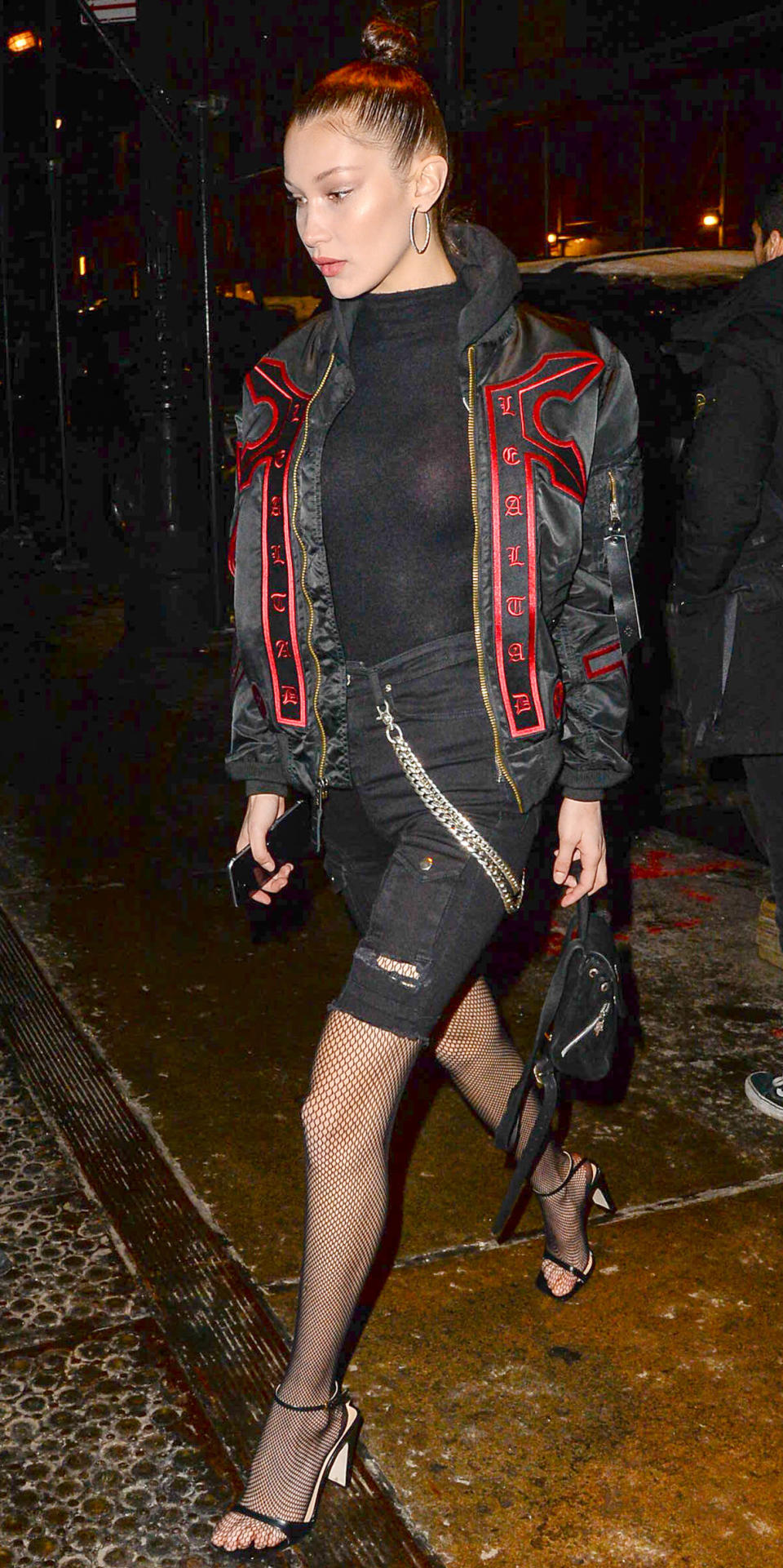 <p>The model donned an all-black ensemble, featuring black jean shorts over fishnet tights and a high-neck bodysuit worn under a hooded bomber with red embroidered details. Large hoops, strappy black heels, and a mini backpack finished off the look.</p>