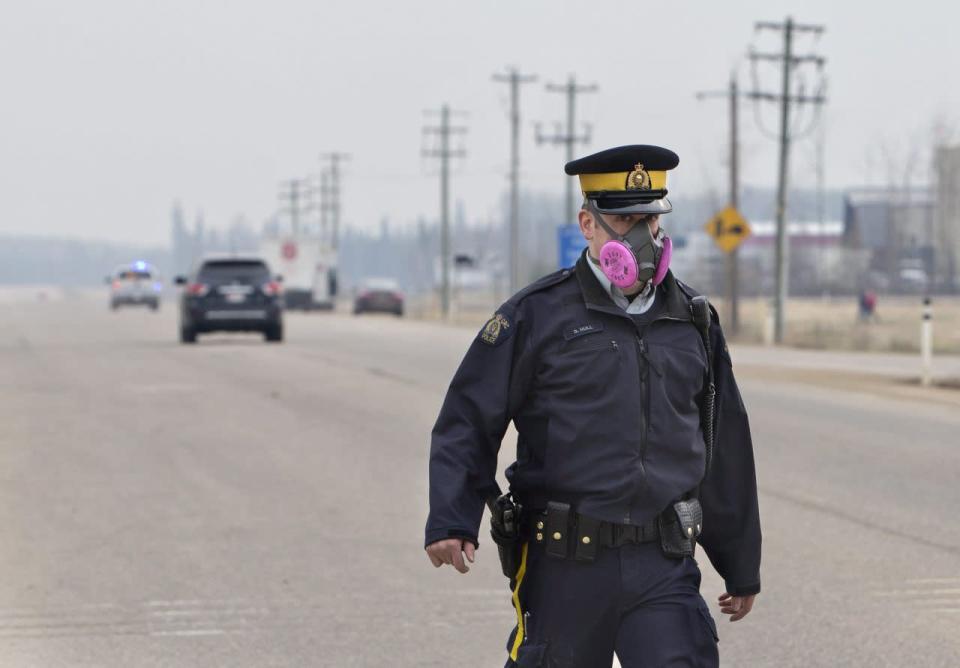 A police officer wears a mask while controlling a roadblock near a wildfire in Fort McMurray, Alberta, Canada on May 5, 2016. Raging wildfires in the Canadian province of Alberta have moved south, forcing three more communities to evacuate and an emergency operations center to move again , aking it far from the devastated oil sands city of Fort McMurray. (Jason Franson/The Canadian Press via AP)