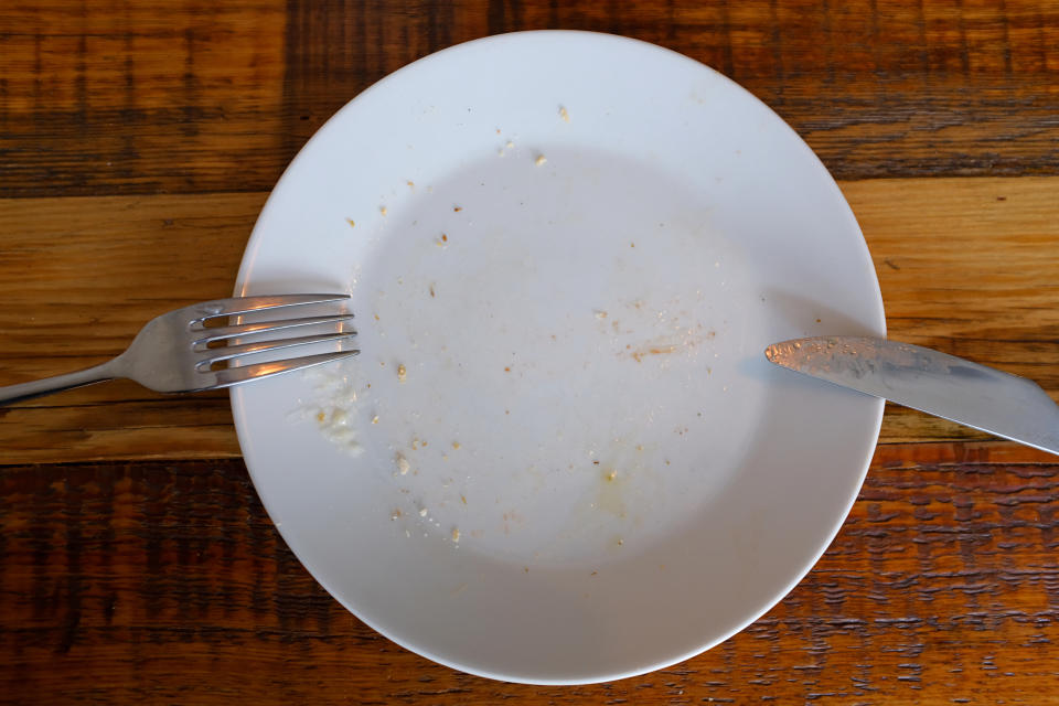 An empty, scraped clean white plate with a fork on the left and a knife on the right, placed on a wooden table