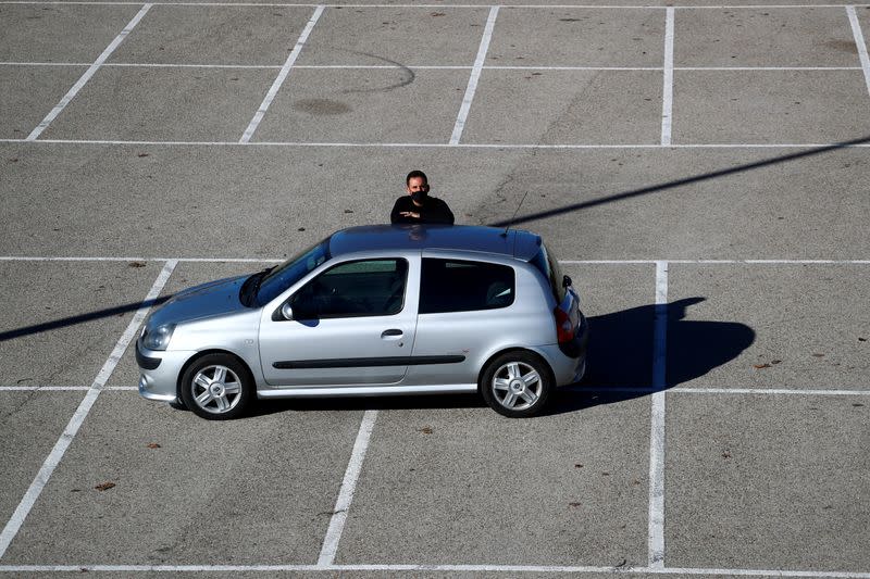 Cristian Lopez poses with his newly-bought 15-year-old second hand car in an empty parking lot in Madrid