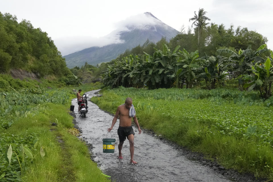 A man walks along a stream near Mayon volcano in Bonga, Legaspi city, Albay province, northeastern Philippines, Saturday, June 10, 2023. Monsoon rains that could be unleashed by an offshore typhoon were complicating worries of villagers threatened by a restive Philippine volcano that has forced thousands of people to flee from their homes.(AP Photo/Aaron Favila)