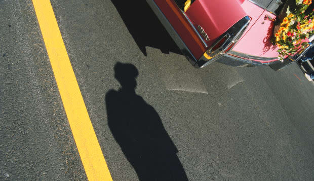 Shadow of woman standing by car with wreath attached to trunk