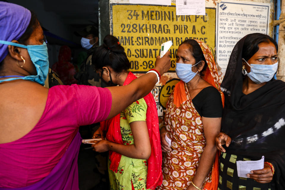 A woman takes the body temperature of a voter standing in a queue to cast her vote outside a polling booth during first phase of elections in West Bengal state in Medinipur, India, Saturday, March 27, 2021. Voting began Saturday in two key Indian states with sizeable minority Muslim populations posing a tough test for Prime Minister Narendra Modi’s popularity amid a months-long farmers’ protest and the economy plunging with millions of people losing jobs because of the coronavirus pandemic. (AP Photo/Bikas Das)