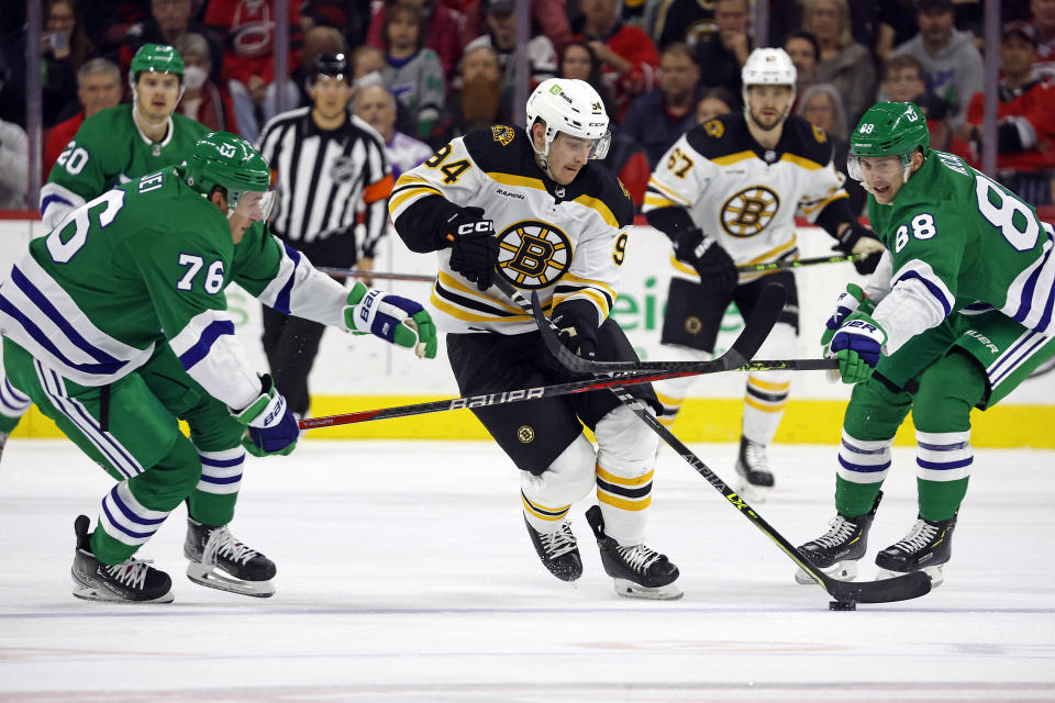 Boston Bruins' Jakub Lauko (94) controls the puck between Carolina Hurricanes' Brady Skjei (76) and Martin Necas (88) during the first period of an NHL hockey game in Raleigh, N.C., Sunday, March 26, 2023. (AP Photo/Karl B DeBlaker)