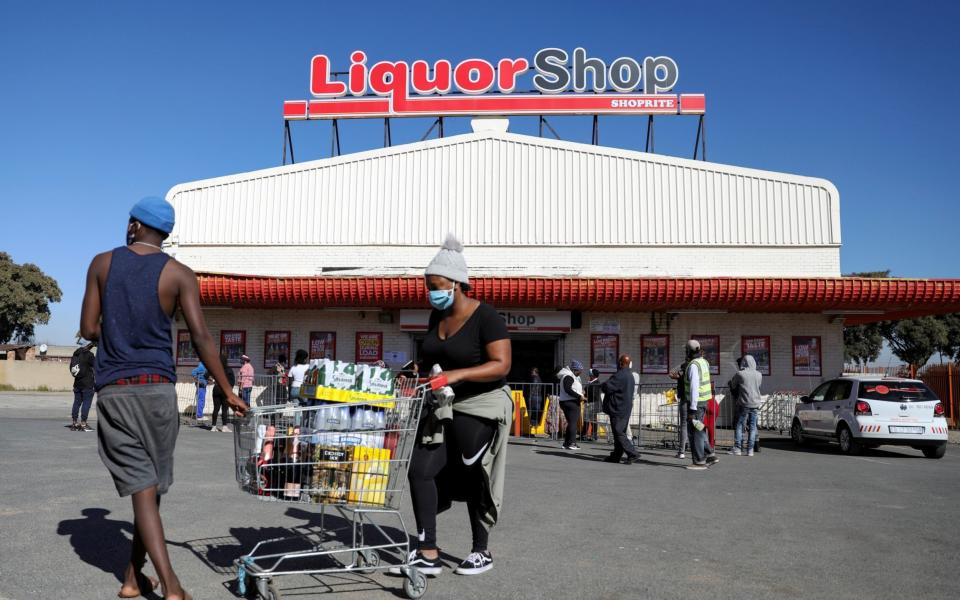 People wearing protective face masks walk with a trolley full of alcohol in front of a liquor store as South Africa lifts a lockdown lasting two months, to try to revive the economy amid the spread of the coronavirus disease (COVID-19), in Soweto, South Africa June 1, 2020. - Siphiwe Sibeko/Reuters