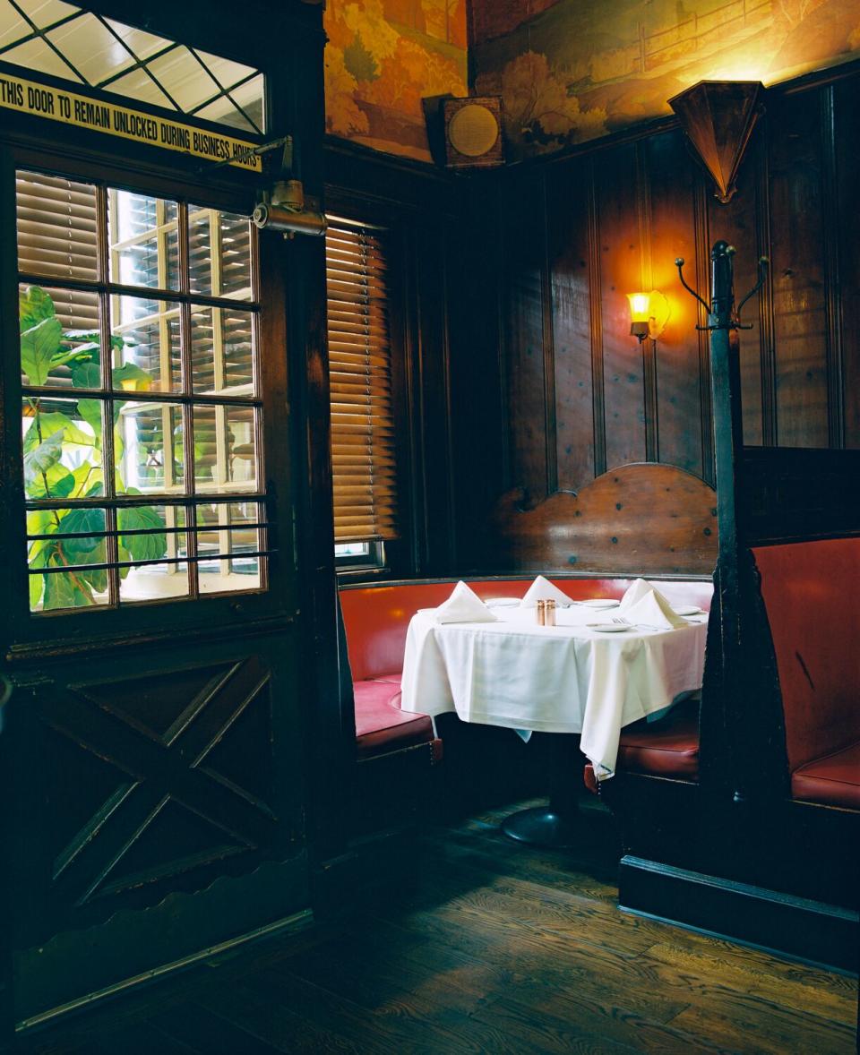 A photo of a corner booth with red upholstery and white table cloths.