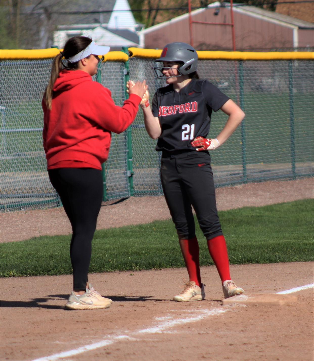 Bedford softball coach Marla Gooding (left) gives a high five to leadoff hitter Sydeny Shammo after hitting an RBI triple against Monroe on Monday, May 9, 2022.