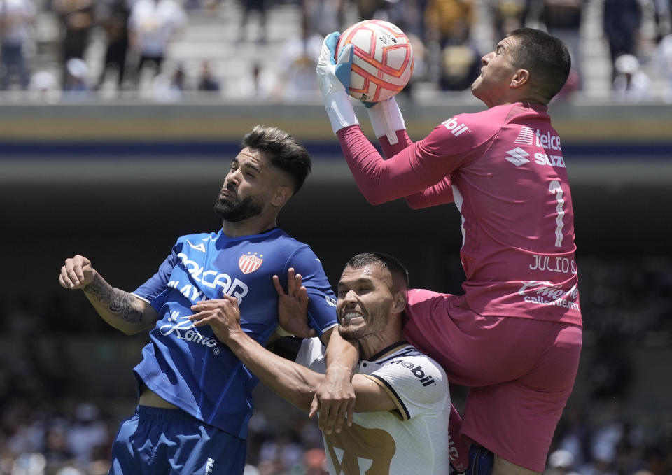 El arquero de Pumas Julio González (derecha) salta sobre su compañero Nicolás Freire (centro) y Milton Giménez de Necaxa en el partido por el torneo Apertura de México, el domingo 17 de julio de 2022. (AP Foto/Moisés Castillo)