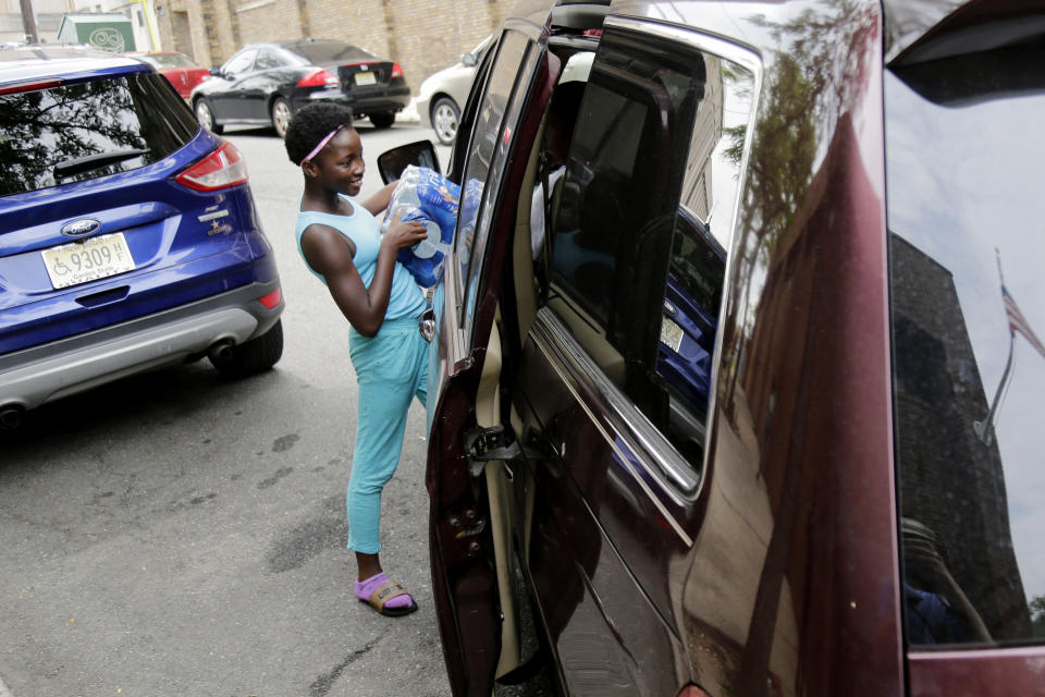 Elaine Younger, 11, loads water in her family's van at the Newark Health Department in Newark, N.J., Wednesday, Aug. 14, 2019. Residents began picking up bottled water on Monday, days after elevated lead levels were found in homes where city-issued filters had been distributed months ago as part of an ongoing effort to combat contamination. (AP Photo/Seth Wenig)