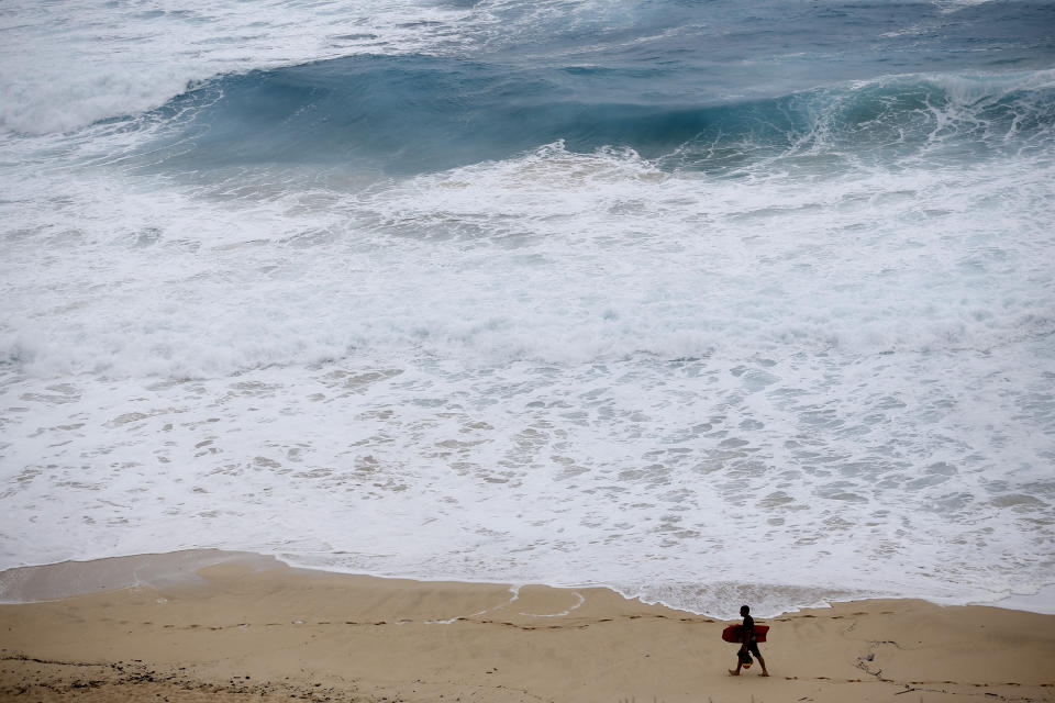 FILE - A boogie boarder walks near the surf at Makapu'u Beach, Friday, Aug. 24, 2018, in Waimanalo, Hawaii, as Hurricane Lane approaches Oahu and large ocean swells impact the coastline. In a report released Wednesday, Dec. 8, 2021, the National Academy of Sciences says to fight climate change the world needs to look into the idea of making the oceans suck up more carbon dioxide. (AP Photo/Marco Garcia, File)