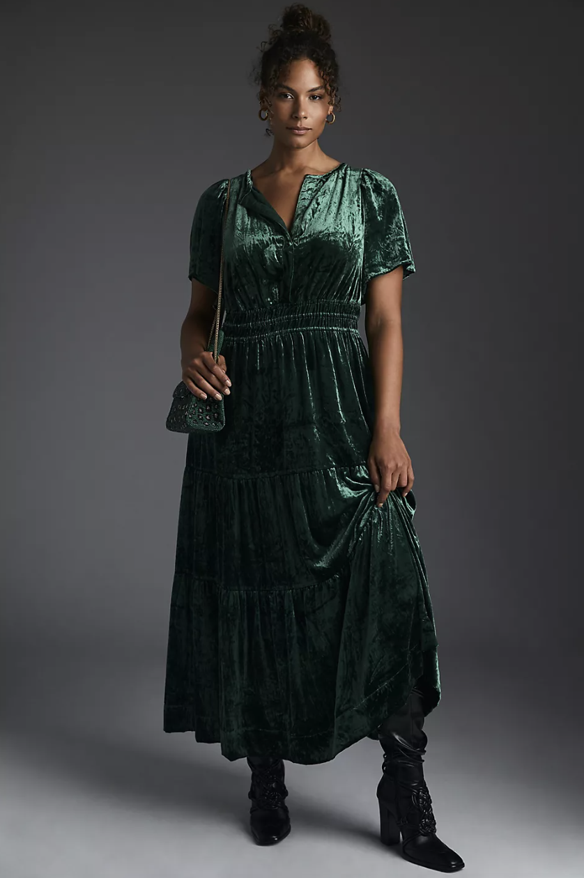 plus size model wearing black boots and The Somerset Maxi Dress: Velvet Edition in green (Photo via Anthropologie)