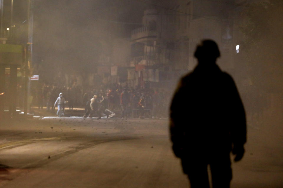 FILE - In this Jan.18, 2021 file photo, demonstrators, background, face police officers during clashes in Ibn Khaldoun City near Tunis. A growing groundswell of youth unrest, tapping into a well of economic frustration, is sweeping Tunisia and worrying its leadership all the way to the top. It is, after all, the country that triggered 2011's Arab Spring revolutions. (AP Photo/Hassene Dridi, File)