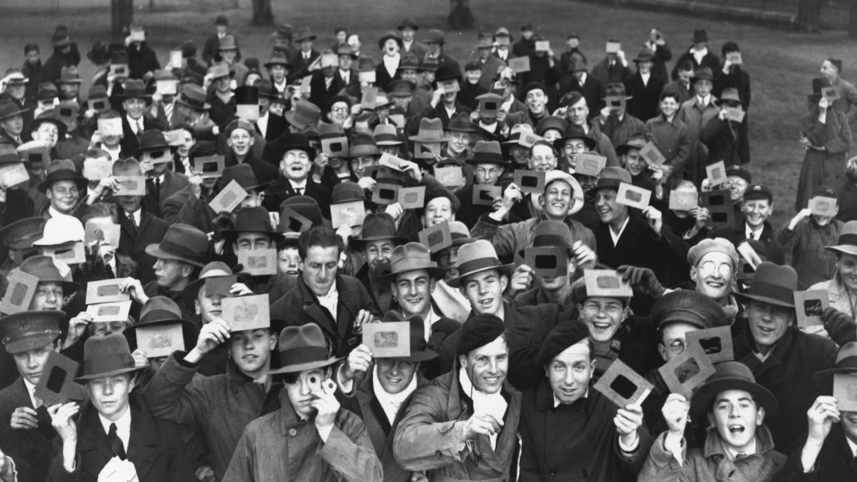  Lots of people with solar eclipse viewers looking up. The image is black and white. 