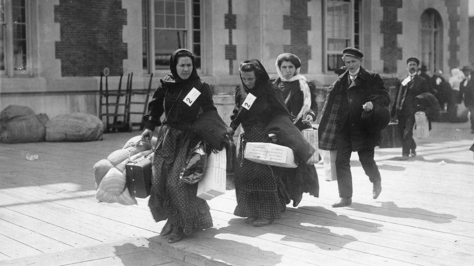 A group of recently arrived immigrants carry their belongings on Ellis Island in the early 1900s. - PhotoQuest/Archive Photos/Getty Images