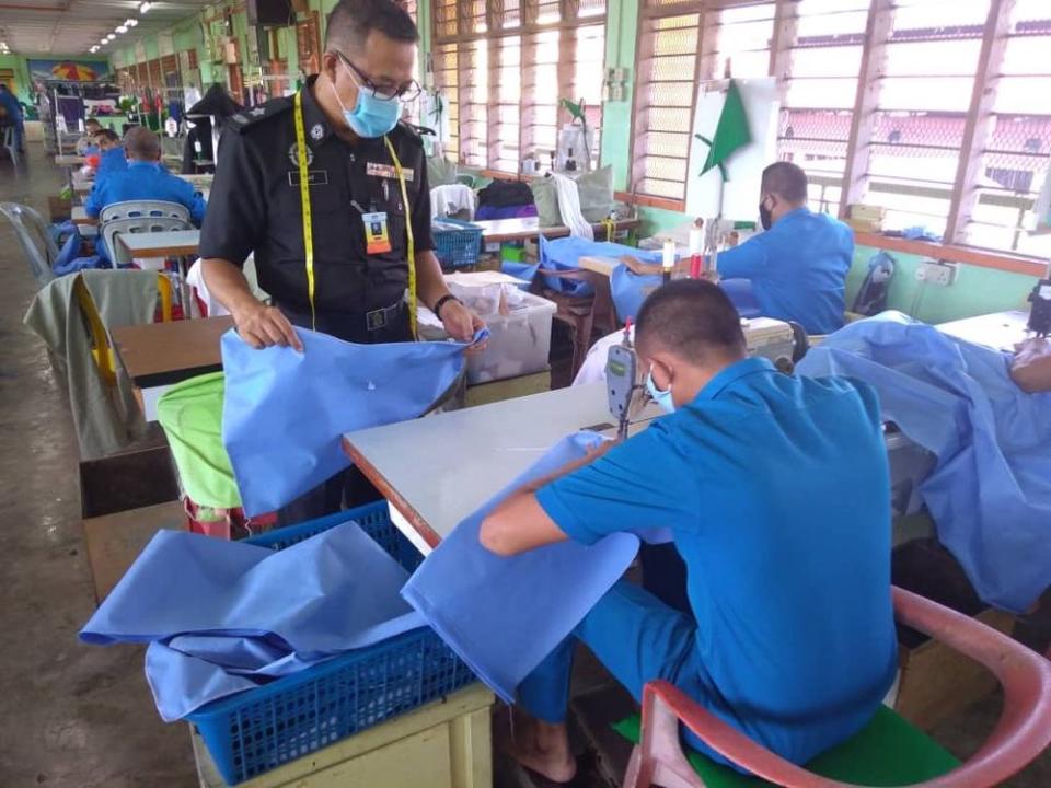 A Kajang Prison inmate sews a PPE suit while his supervisor observes him. — Picture courtesy of Twitter/Malaysian Prisons Department