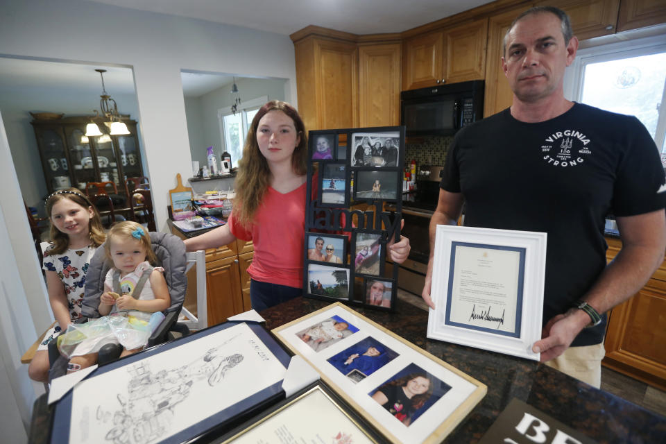 In this May 22, 2020, photo, Jason Nixon, right, holds a letter from President Donald Trump as he poses with his children, Mackenzie, left, Madilyn, second from left and Morgan as they display memorabilia from last years shooting that took the life of Kate Nixon at their home in Virginia Beach, Va. As the shooting's one-year anniversary approaches this weekend, some of the victim's family members say the rampage is effectively forgotten. (AP Photo/Steve Helber)