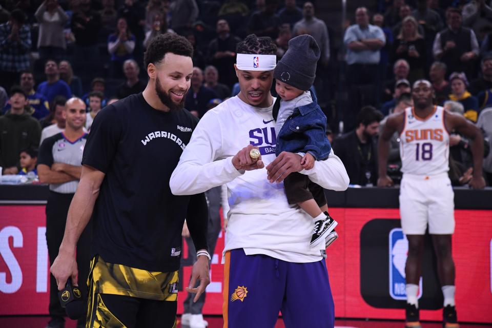 Suns guard Damion Lee checks out his NBA championship ring with his son and brother-in-law, Warriors guard Stephen Curry, who presented him the ring before Tuesday's Jan. 10 game at Chase Center between Phoenix and Golden State.