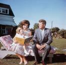 <p>Known for her classic style during her marriage to John F. Kennedy, Jackie reads to her daughter Caroline at the family's summer home in a classically-cut floral-patterned dress and matching pink pumps while the Senator looks on.<br></p>