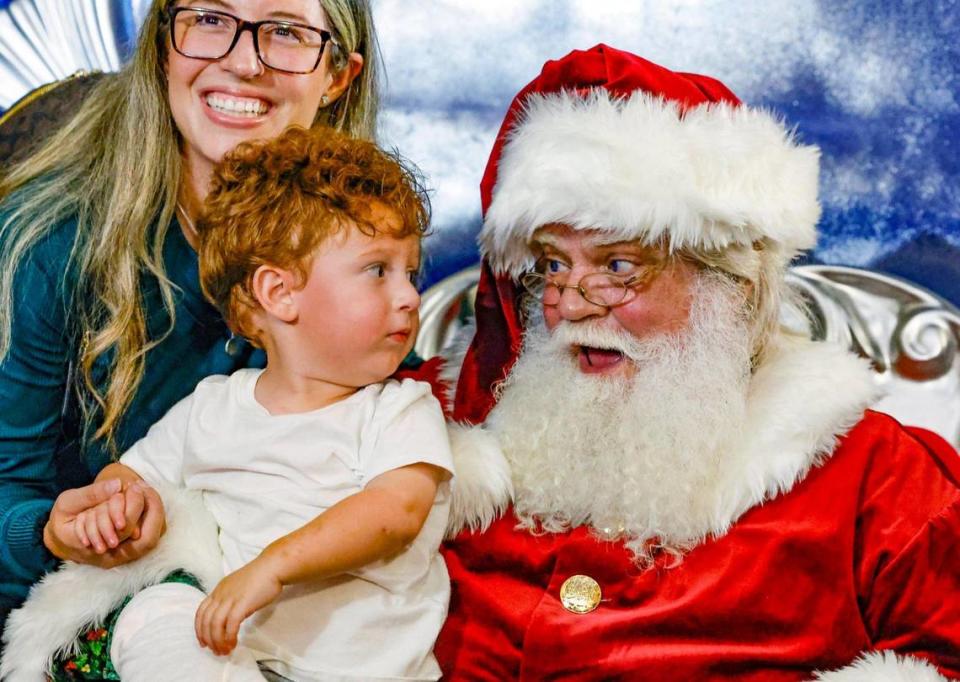 Santa Claus charla con Cole Dimarzo, de 2 años, mientras su madre Giovanna Dimarzo reacciona durante la experiencia en la noche de apertura de Christmas Wonderland en el Tropical Park, en Miami, el viernes 17 de noviembre de 2023.
