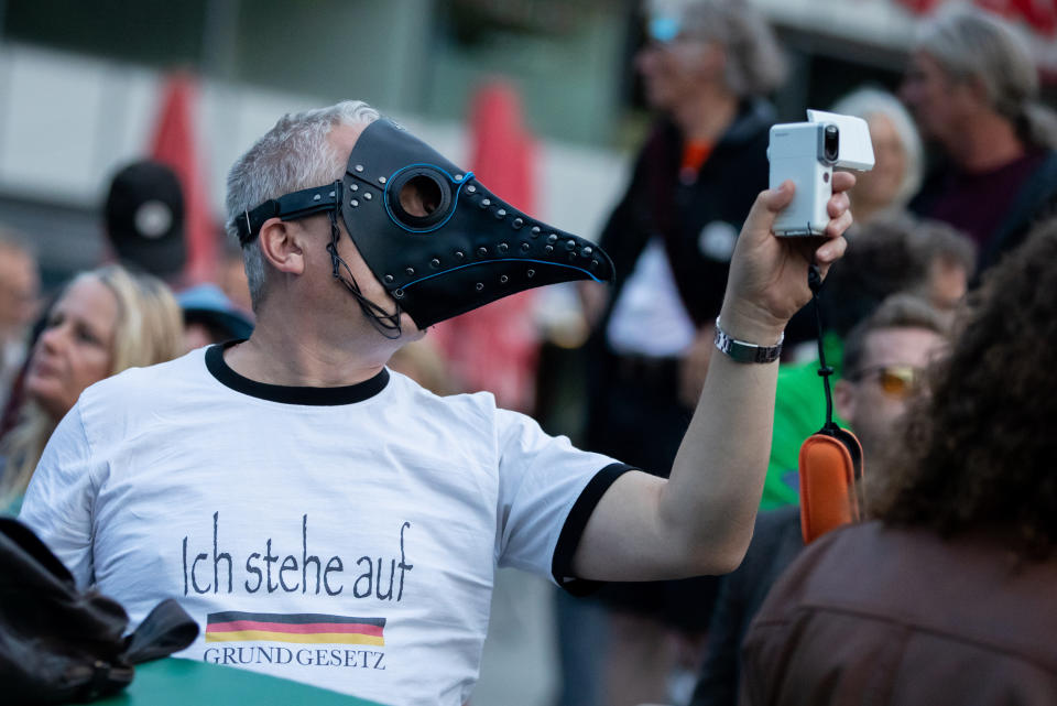 A man with a beak mask holds a camera at a rally against the corona measures on Thursday, Aug. 27, 2020. The rally with the motto "Berlin invites Europe! - Berlin Invites Europe!" is to be the prelude to the demonstration against corona restrictions on Saturday. Police in Berlin have requested thousands of reinforcements from other parts of Germany to cope with planned protests at the weekend by people opposed to coronavirus restrictions. (Christoph Soeder/dpa via AP)