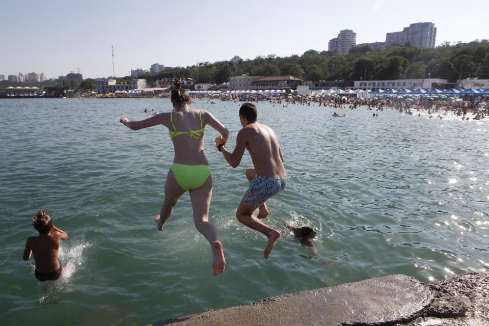 A couple jump into a water as they enjoy the beach in the Black Sea in Odessa, Ukraine, Saturday, July 4, 2020. Tens of thousands of vacation-goers in Russia and Ukraine have descended on Black Sea beaches, paying little attention to safety measures despite levels of contagion still remaining high in both countries. (AP Photo/Sergei Poliakov)
