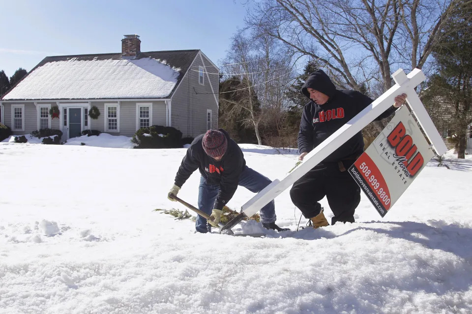 Kevin Thompson, left, and Dave Garro of Bold Moves Real Estate dig a real estate sign out of the snow pack in the front yard of a property on Crestfield Street in Mattapoisett, Mass. (Credit: Stephan Savoia)