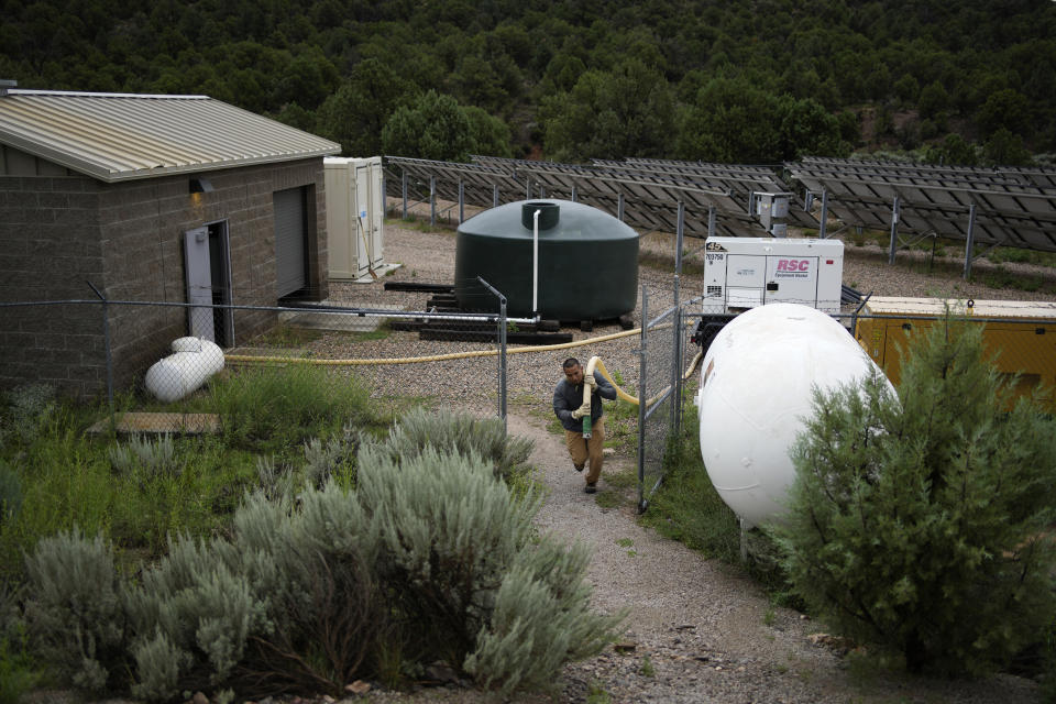 Garnett Querta carries a hose as he fills his water truck on the Hualapai reservation Monday, Aug. 15, 2022, near Peach Springs, Ariz. The divvying up between Colorado River Basin states never took into account Indigenous Peoples or many others, and from the start the calculation of who should get what amount of that water may never have been balanced. (AP Photo/John Locher)