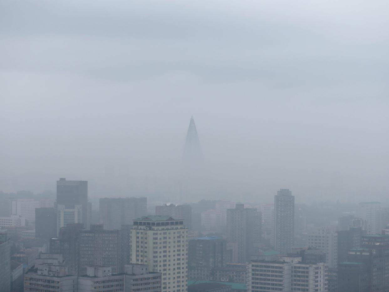 The Ryugyong Hotel rises above the city skyline, shrouded by a layer of mist.