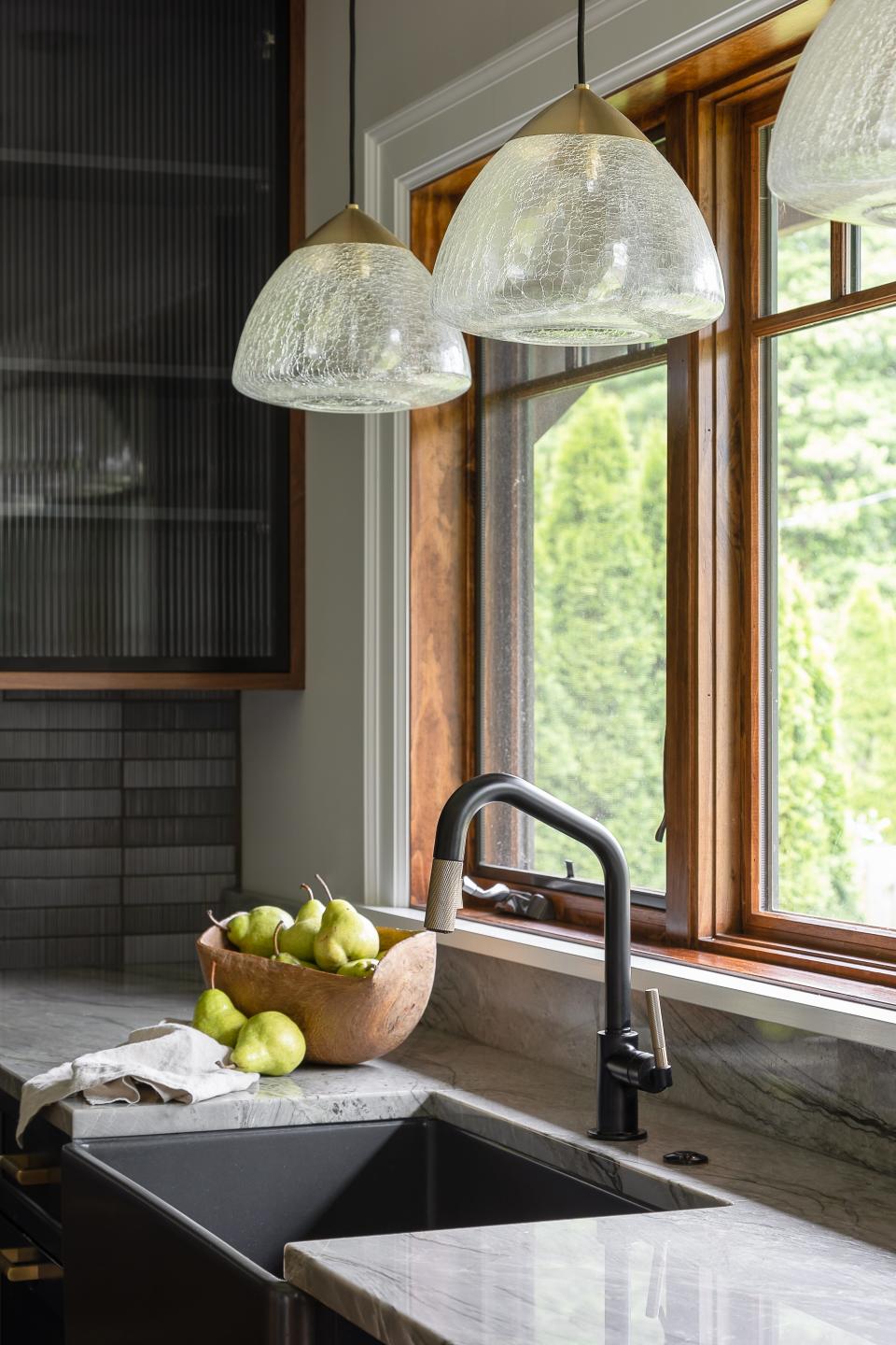 Pendant lights hang above a black farmhouse sink in this remodeled Dutch Colonial Revival home in Audubon Park that was built in 1930.