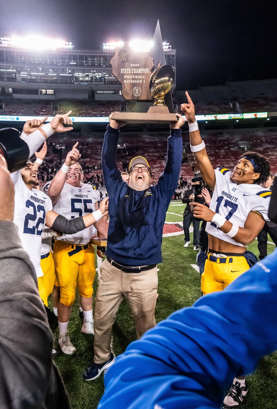 Marquette head football coach Keith Klestinski hoists the gold trophy after winning the WIAA Division 1 state championship, 27-10, over Franklin Friday at Camp Randall Stadium.