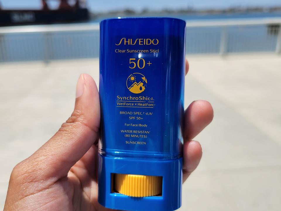 A person's hand holding Shiseido's clear sunscreen stick.