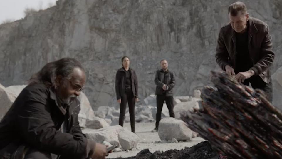Four people surround a piece of alien debris in a quarry