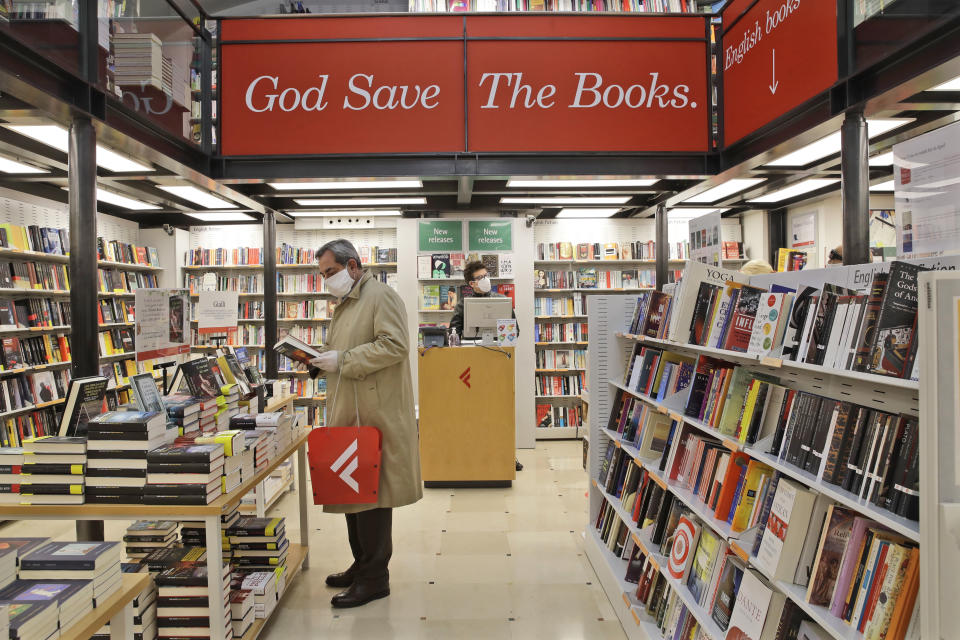 A man holds up a book inside an open bookstore in Rome, Monday, April 20, 2020. In Italy, bookstores, stationary stores and shops selling baby clothes and supplies were allowed to open nationwide last Tuesday, provided they could maintain the same social-distancing and sanitary measures to prevent the spread of COVID-19 required in supermarkets. (AP Photo/Alessandra Tarantino)