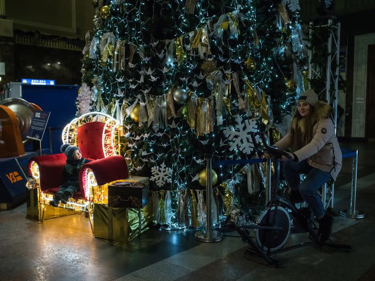 En Kiev, Ucrania, una mujer pedalea un generador de bicicleta para alimentar las luces de un árbol de Navidad expuesto en la estación de ferrocarril.