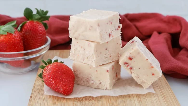A stack of white strawberry fudge pieces next to whole strawberries