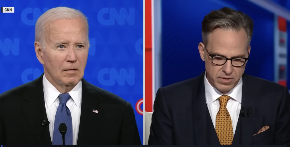 Joe Biden and Jake Tapper engage in a discussion on CNN, with Biden appearing thoughtful and Tapper looking down, reviewing notes