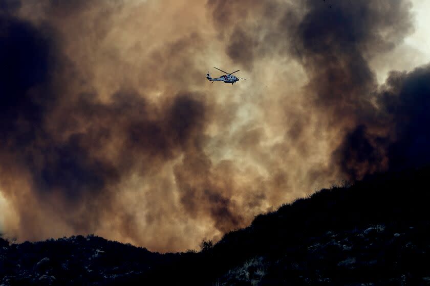 HEMET, CALIF. - SEP 6, 2022. A firefighting helicopter is dwarfed by the plume of the Fairview fire along Batista Road near Hemet on Tuesday, Sep. 6, 2022. (Luis Sinco / Los Angeles Times)