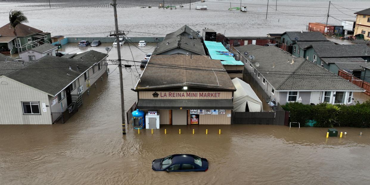 This aerial photograph shows a car and market shop in floodwaters in Pajaro, California on Saturday, March 11, 2023. - Residents were forced to evacuate in the middle of the night after an atmospheric river surge broke the the Pajaro Levee and sent flood waters flowing into the community.