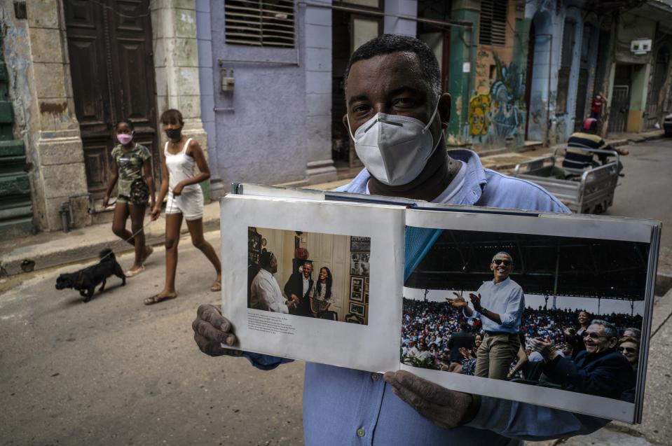 Con mascarilla en medio de la pandemia del nuevo coronavirus, Cristóbal Márquez, dueño de "Cristóbal's", el restaurante donde almorzaron Michelle y Barack Obama durante su visita a Cuba en 2016, muestra el libro realizado por el fotógrafo de la Casa Blanca Pete Souza, en La Habana, Cuba, el jueves 22 de octubre de 2020. (AP Foto/Ramón Espinosa)