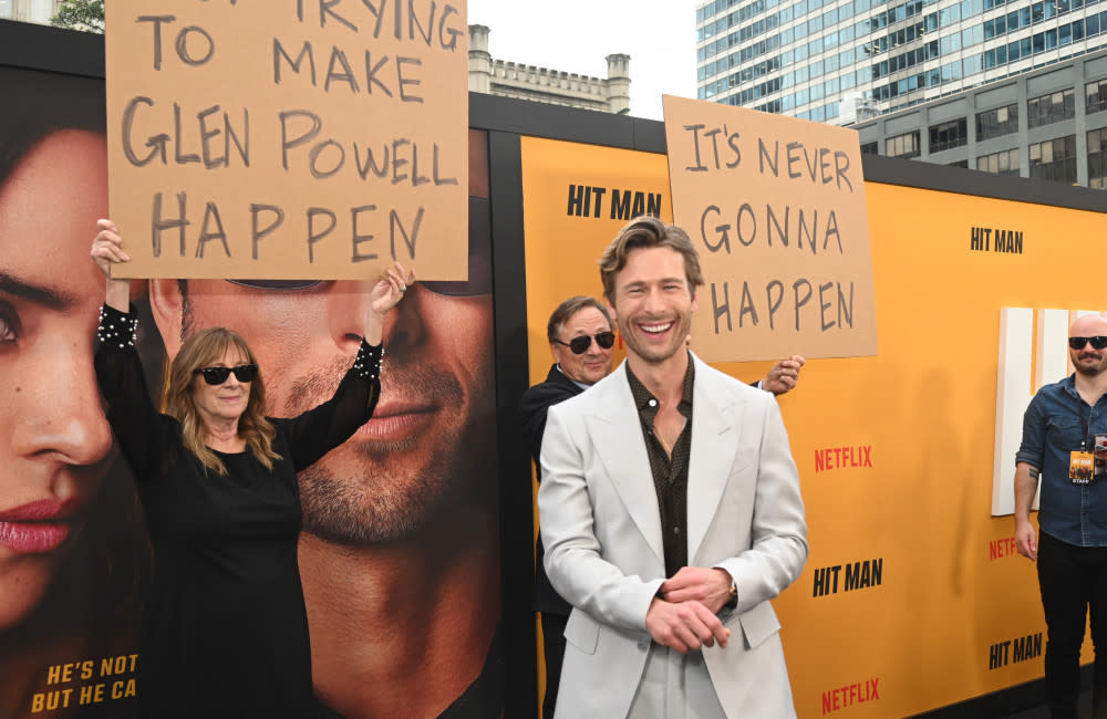 Glen Powell did not seem to mind when his parents held up signs at the red carpet premiere of his movie Hit Man credit:Bang Showbiz