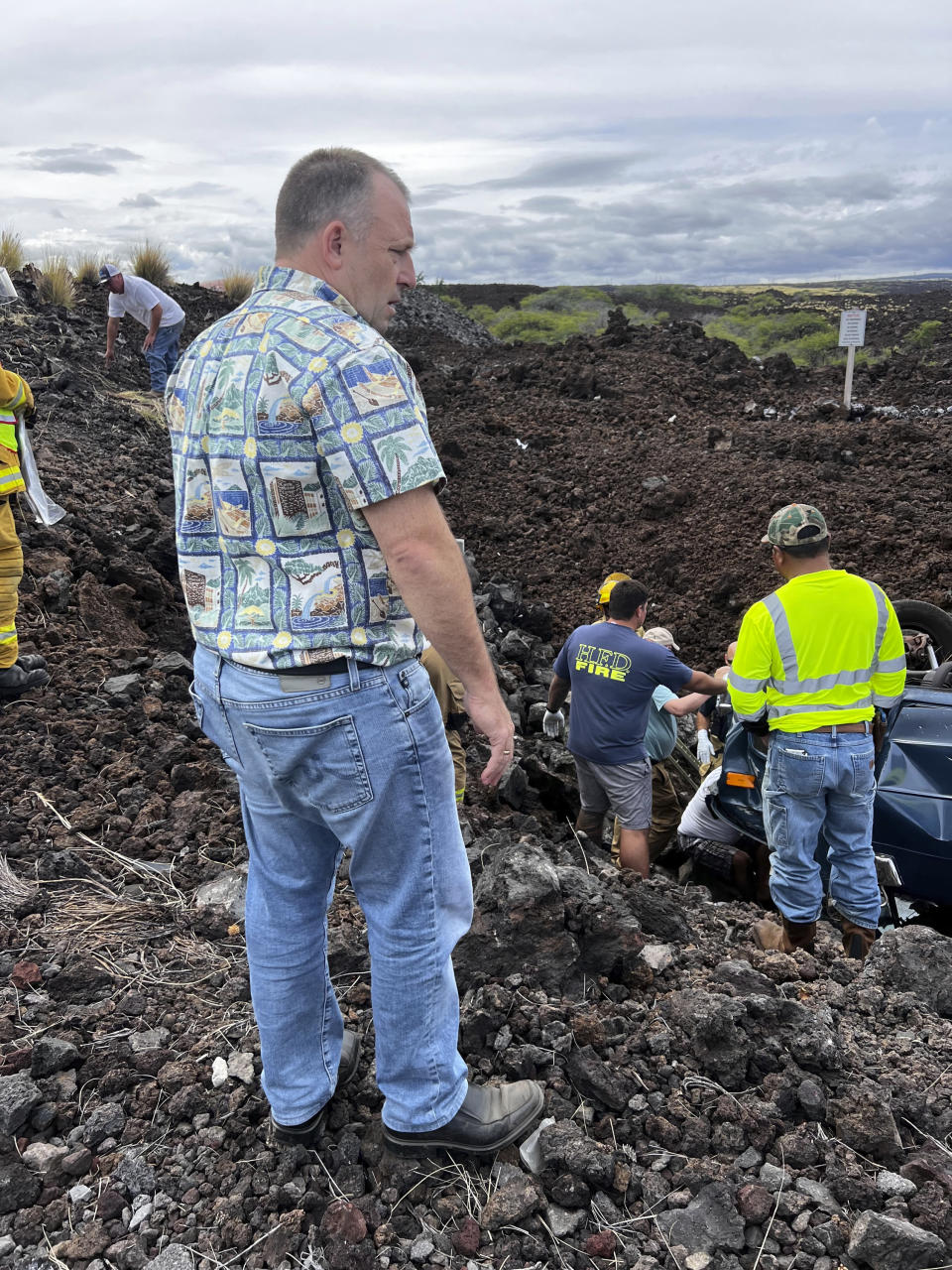 Hawaii Gov. Josh Green, left, looks under a flipped vehicle as he stops to help at the scene of an overturned vehicle in Waikoloa, Hawaii, Thursday, May 18, 2023. Gov. Green, who is also a physician, was one of the people who stopped to help when his security detail spotted a vehicle upside down in a lava field Thursday while en route to a Big Island event. (Reece Kainoa Kilbey/Office of the Governor, State of Hawai'i via AP)