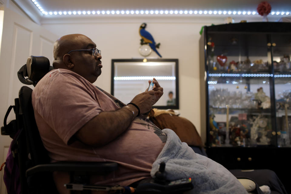 Thirugnanam Sureshan, 50, whose disabilities require round-the-clock care, holds up his insulin pen as he discusses concerns about cost of living increases at his home in Bexhill, East Sussex, England, Wednesday, Nov. 9, 2022. Sureshan has a rare condition called Charcot foot which affects the bones, joints and tissues in his foot. He also has thyroid problems and an eye condition. Because of his condition, he doesn't cope well with the cold. (AP Photo/David Cliff)