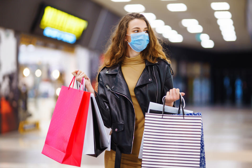 Young  woman in protective medical mask with shopping bags using her phone. Purchases, black friday, discounts, sale concept. Online shopping concept.