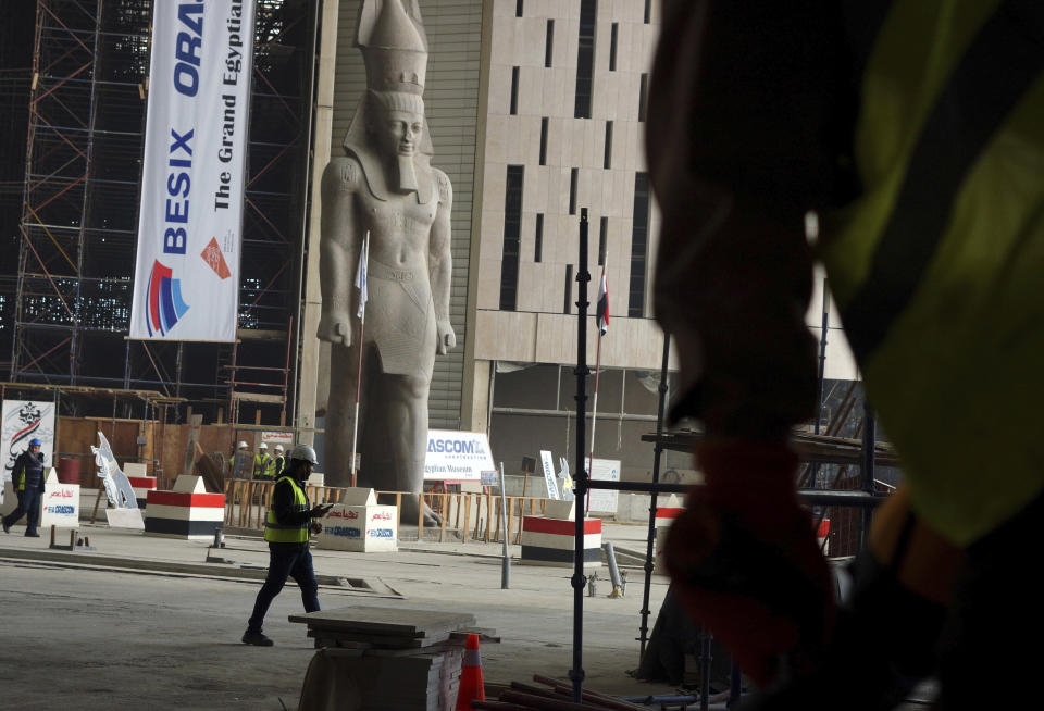 In this Sunday, Dec. 16, 2018 photo, work continues in the shadow of a statue of Pharaoh Ramses II, at the Grand Egyptian Museum, under construction in Giza, Egypt. Thousands of Egyptians are laboring in the shadow of the pyramids to erect a monument worthy of the pharaohs. The Grand Egyptian Museum has been under construction for well over a decade and is intended to show off Egypt’s ancient treasures while attracting tourists to help fund its future development. (AP Photo/Amr Nabil)