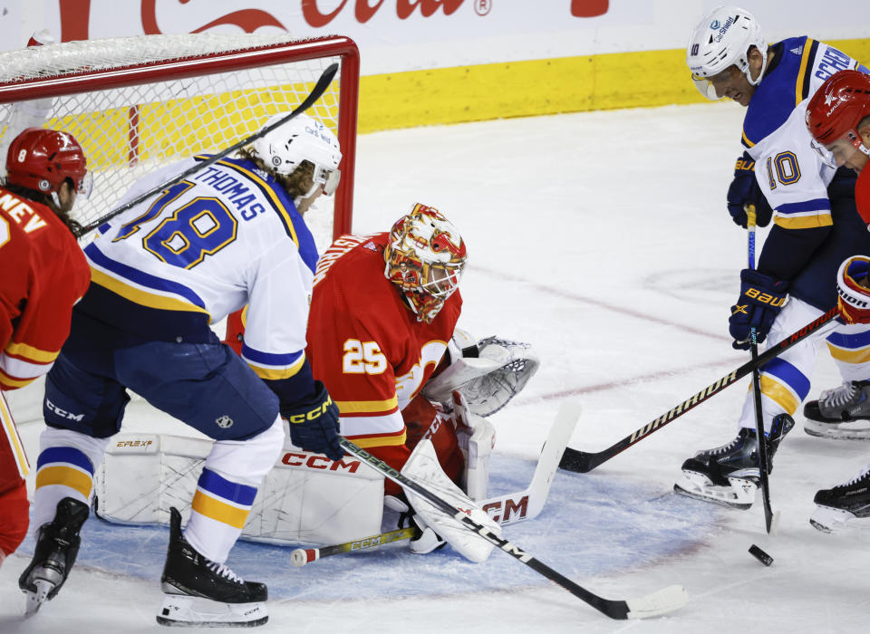 St. Louis Blues forward Robert Thomas, left, and forward Brayden Schenn, right, reach for a lose puck as Calgary Flames goalie Jacob Markstrom looks on duirng the second period of an NHL hockey game in Calgary, Alberta, Thursday, Oct. 26, 2023. (Jeff McIntosh/The Canadian Press via AP)