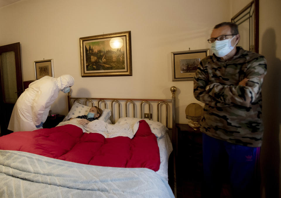 Doctor Luigi Cavanna visits COVID-19 patient Maria Teresa Orsi as her husband Maurizio stands by, in their home, in Monticelli d'Ongina, near Piacenza, Italy, Wednesday, Dec. 2, 2020. (AP Photo/Antonio Calanni)