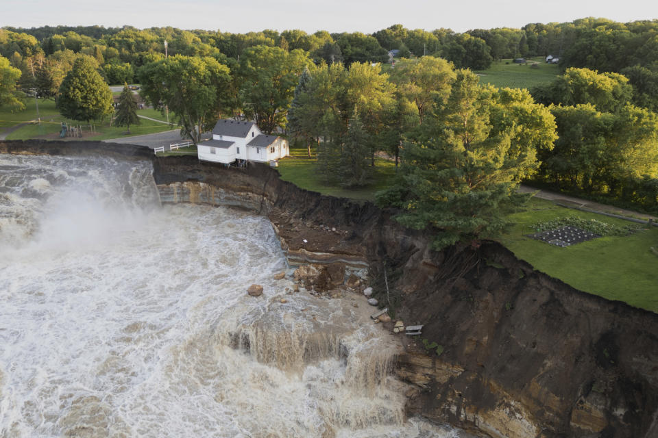 This drone photo provided by AW Aerial shows a home as it teeters before partially collapsing into the Blue Earth River at the Rapidan Dam in Rapidan, Minn., Tuesday, June 25, 2024. (Andrew Weinzierl/AW Aerial via AP)