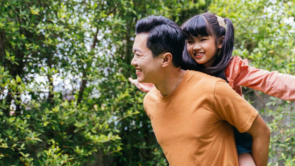 young father giving his daughter a piggyback ride and smiling in an outdoor park