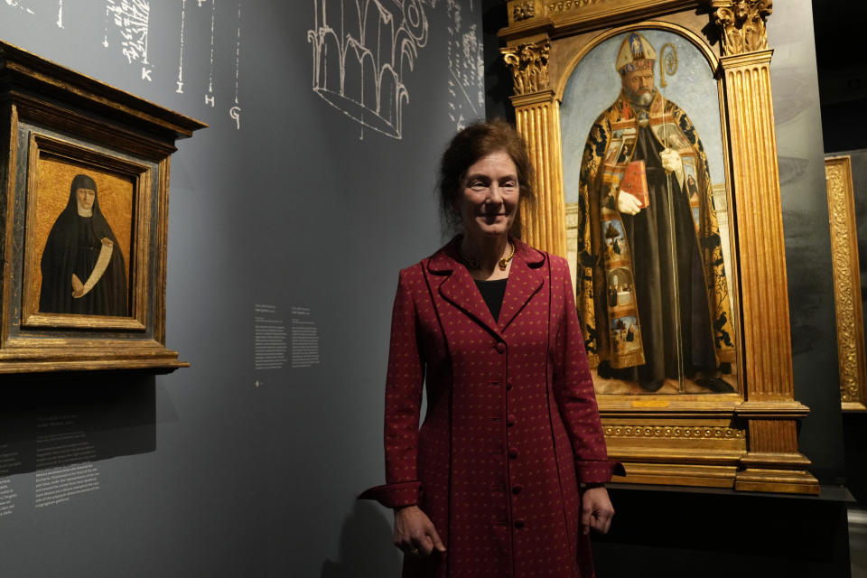 The exhibition curator Machtelt Bruggen Israels poses next to Italian artist Piero della Francesca's paintings on the occasion of the inauguration of the exhibit "Piero della Francesca. Il Polittico Agostiniano riunito" (Piero della Francesca. The Augustinian Polyptych reunited) at Milan's Poldi Pezzoli museum, Italy, Tuesday, March 19, 2024. The Augustinian altarpiece originally comprised 30 sections in a polyptych, was dismantled after the Augustinians moved churches and eventually sold off. Only eight of the sections remain as individual paintings owned by museums in New York, Washington, D.C., London, Milan and Lisbon, Portugal. (AP Photo/Antonio Calanni)