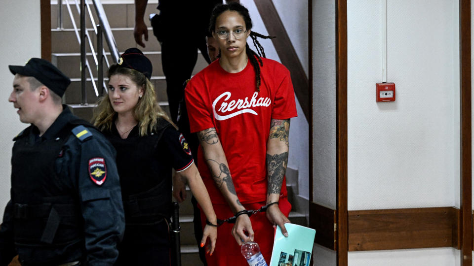 Brittney Griner, wearing handcuffs, at the bottom of a stairway.